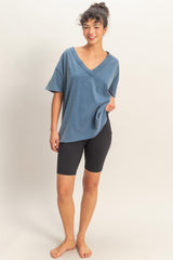 woman wearing a blue oversized v-neck t-shirt with black biker shorts and standing barefoot