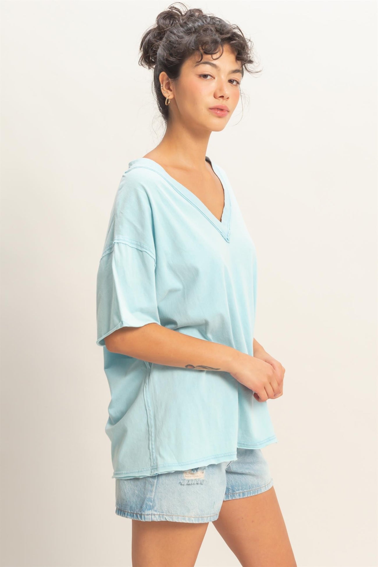 woman wearing a light blue oversized v-neck t-shirt with rolled short sleeves and denim shorts
