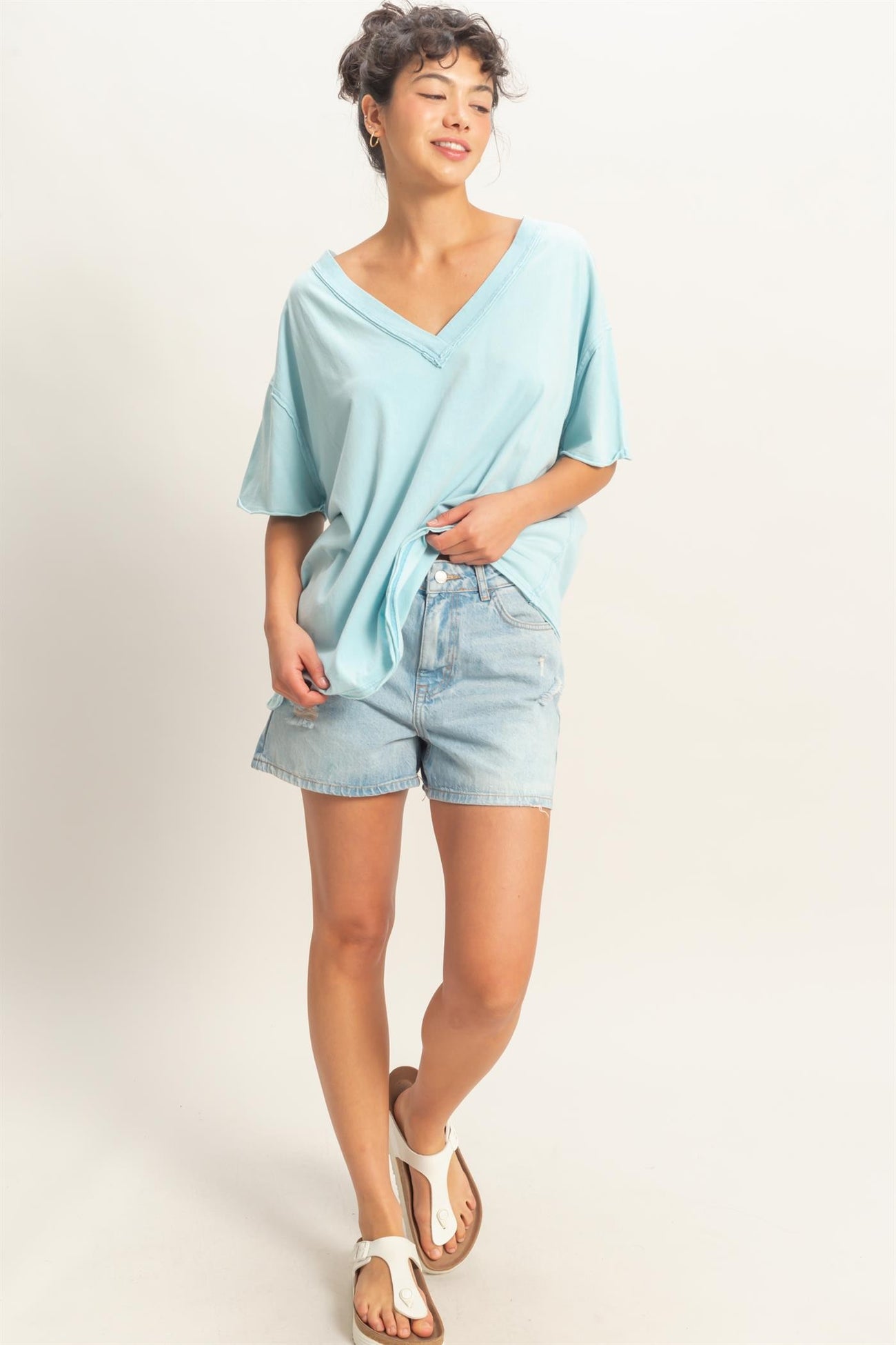 woman wearing a light blue oversized v-neck t-shirt and denim shorts, standing with one hand on her hip