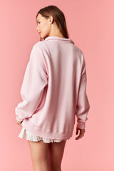 woman wearing a oversized light pink sweatshirt with ribbed hem and cuffs, styled with a white ruffled skirt.