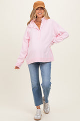 woman wearing a pink oversized maternity pullover with a collar and blue jeans, showcasing her baby bump