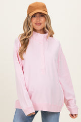 woman wearing a light pink maternity sweatshirt with a high neckline and long sleeves, styled with a tan cap
