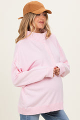 woman wearing a light pink maternity pullover sweatshirt with a high collar and relaxed fit, showing her baby bump