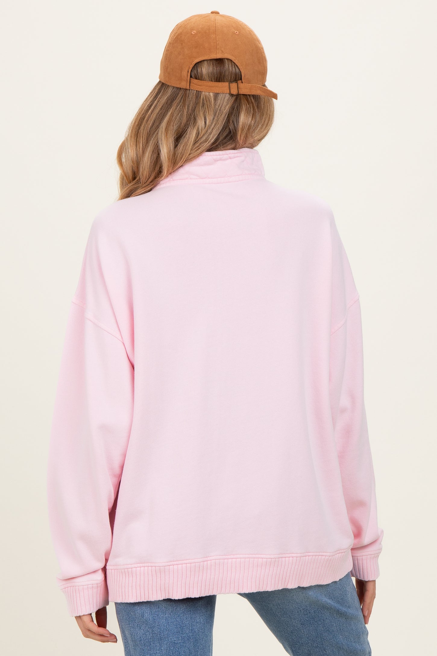 woman wearing a light pink oversized maternity sweatshirt, viewed from the back, with a brown cap