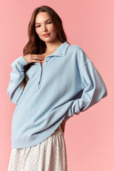 woman wearing a light blue oversized pullover sweatshirt with a collar and paired with a white polka dot skirt