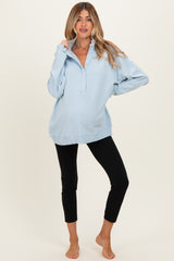 woman wearing a light blue maternity pullover with a collar, paired with black leggings and showing her baby bump