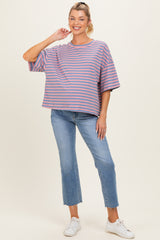 woman wearing a striped purple and pink maternity top with loose fit and blue jeans, smiling and standing with one hand on her hip