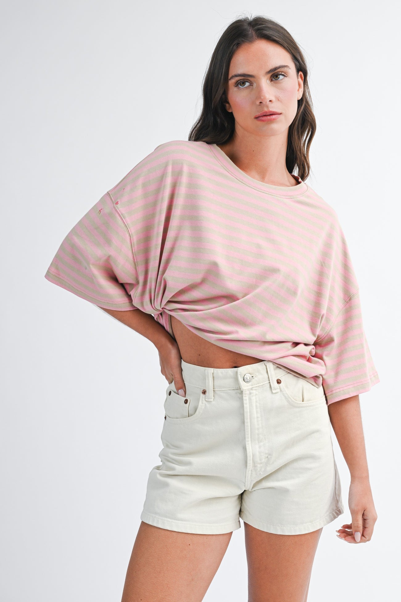 woman wearing a pink striped oversized t-shirt with knotted detail and cream-colored denim shorts