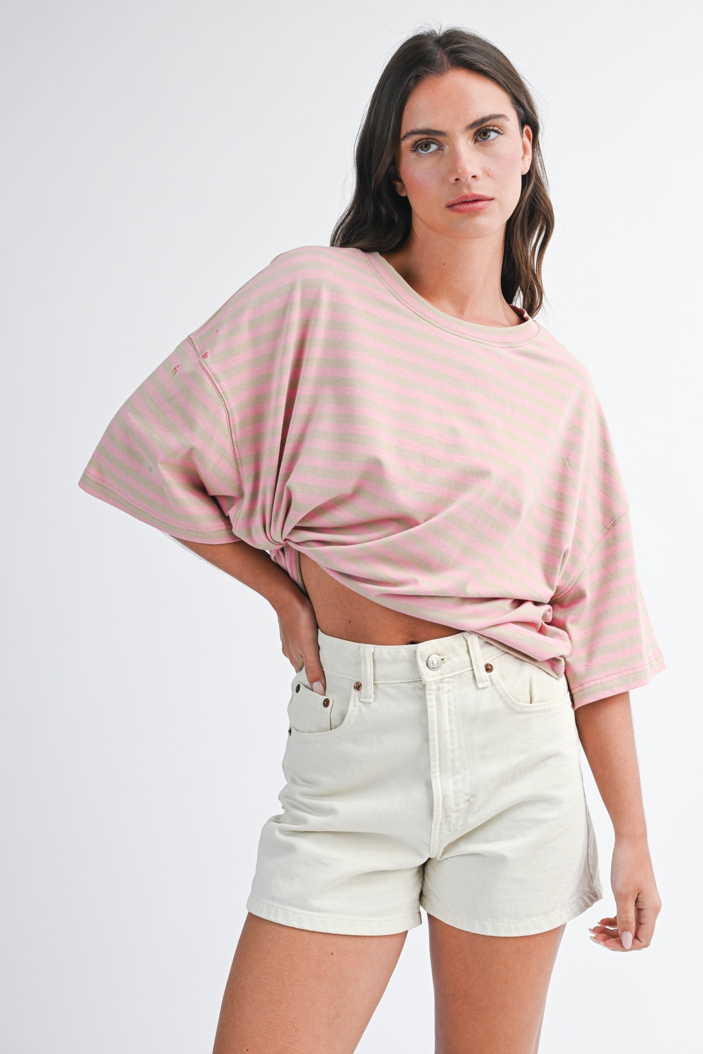 woman wearing a pink striped oversized t-shirt with knotted detail and cream-colored denim shorts