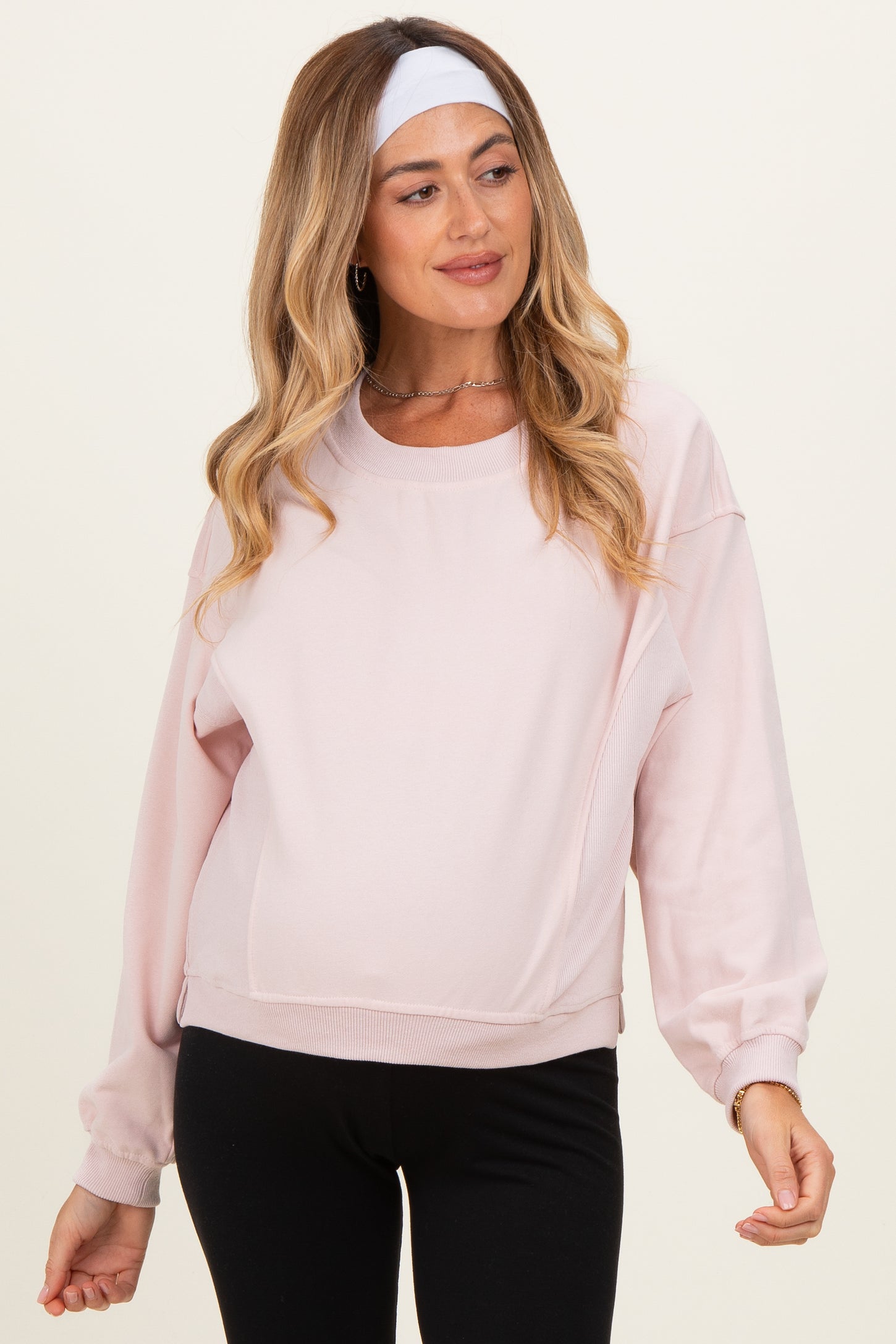 woman wearing a light pink maternity sweatshirt with long sleeves and a relaxed fit, showcasing a visible baby bump
