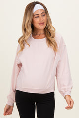woman wearing a light pink maternity sweatshirt with long sleeves and a relaxed fit, showcasing a visible baby bump