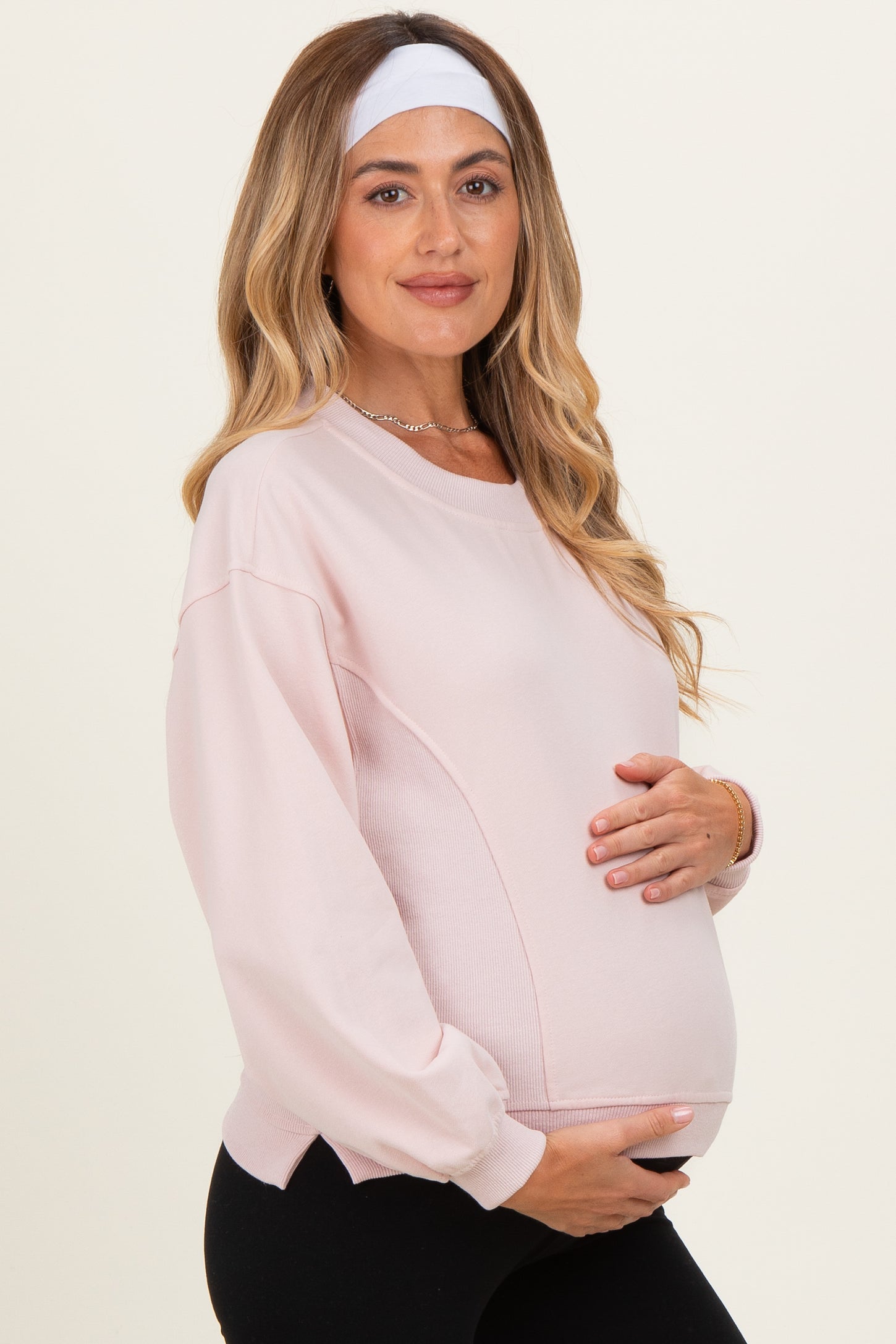woman wearing a light pink maternity sweatshirt and holding her baby bump