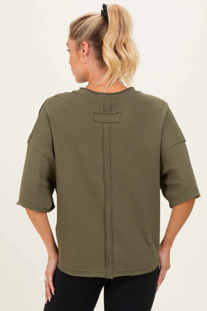 woman wearing an olive green maternity top with a relaxed fit and raw hem details, showcasing the back style