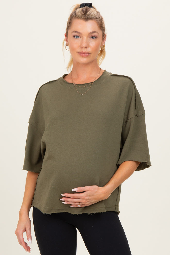 woman wearing an olive green oversized maternity top with a textured hem and holding her baby bump