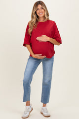 woman wearing a red maternity top and blue jeans, smiling and holding her baby bump