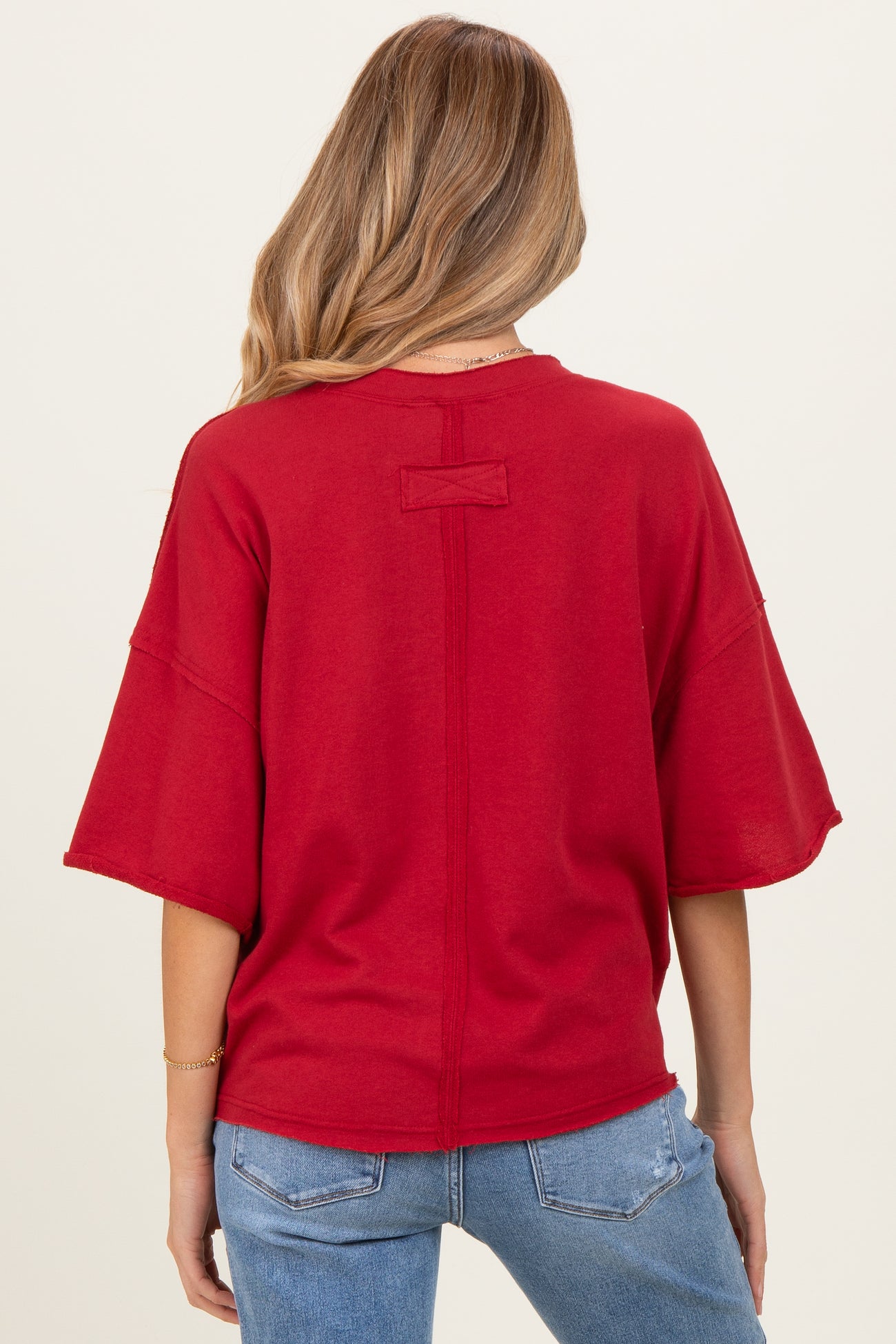 woman wearing a red oversized maternity top with short sleeves and a relaxed fit, viewed from the back