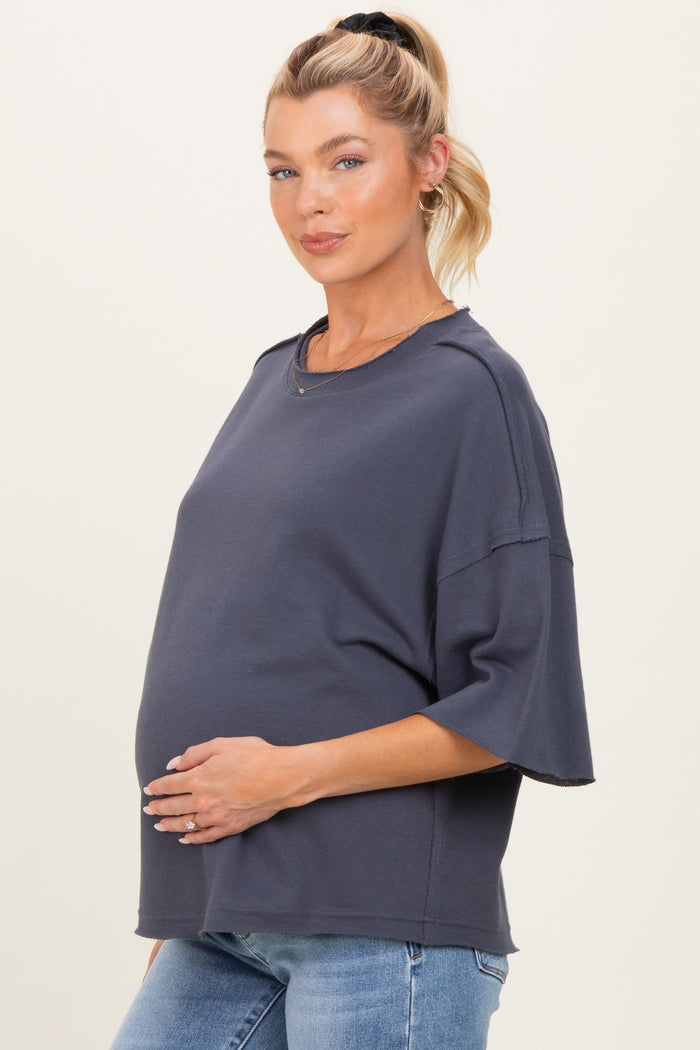 woman wearing a dark gray maternity top with short sleeves and a relaxed fit, gently holding her baby bump