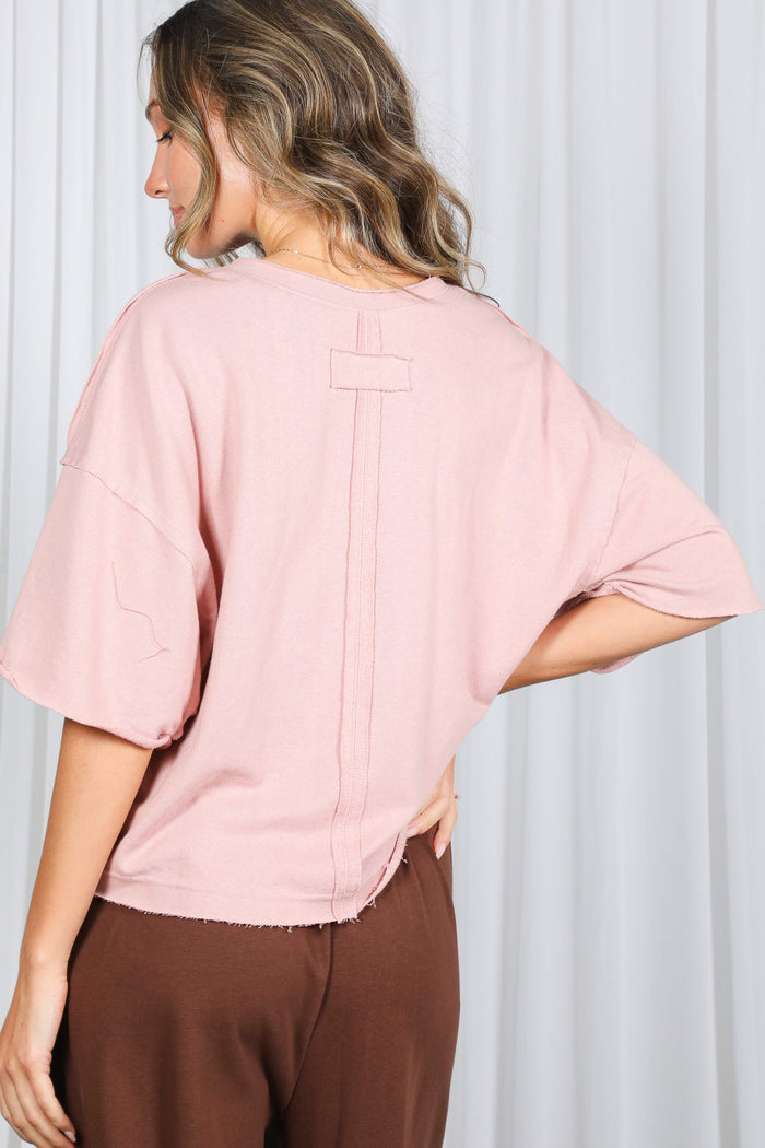 woman wearing a blush pink oversized short sleeve top with a raw hem and back seam detail