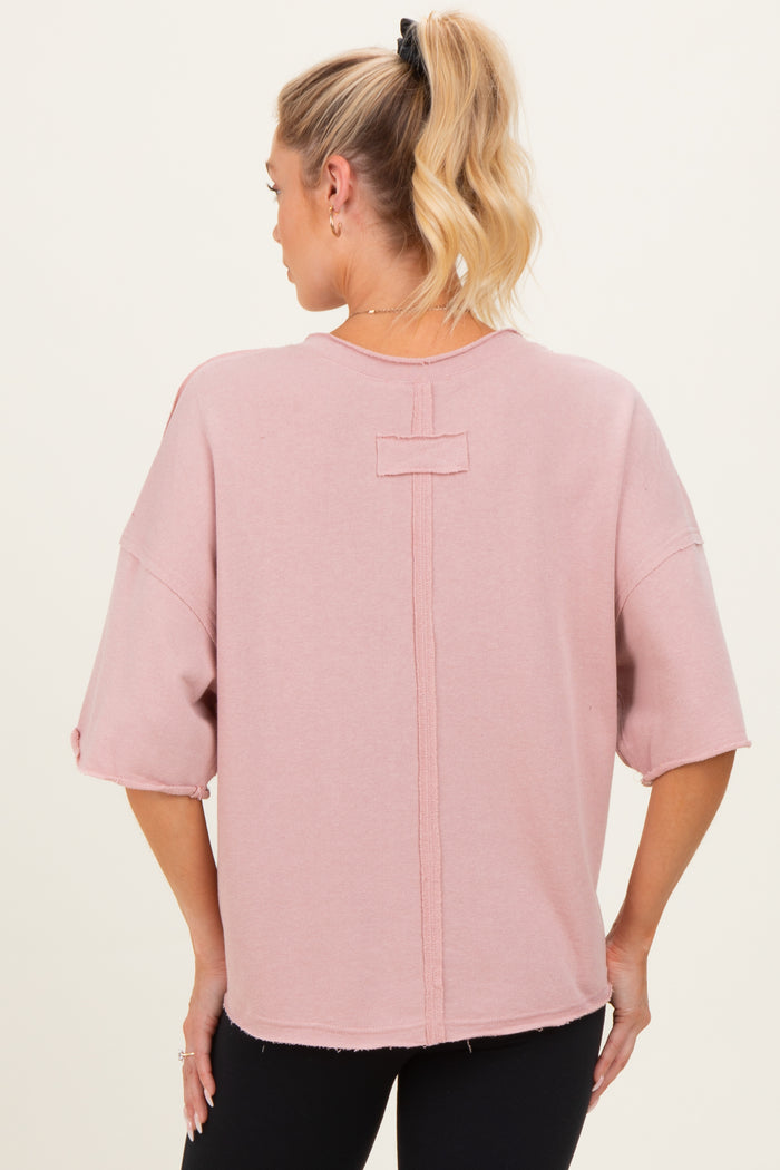 woman wearing a pink oversized maternity top with a relaxed fit and back seam detail