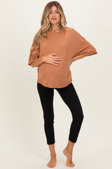 woman wearing a rust colored oversized maternity top and black leggings, holding her baby bump