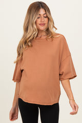 woman wearing a rust-colored oversized maternity top with short sleeves and a visible baby bump