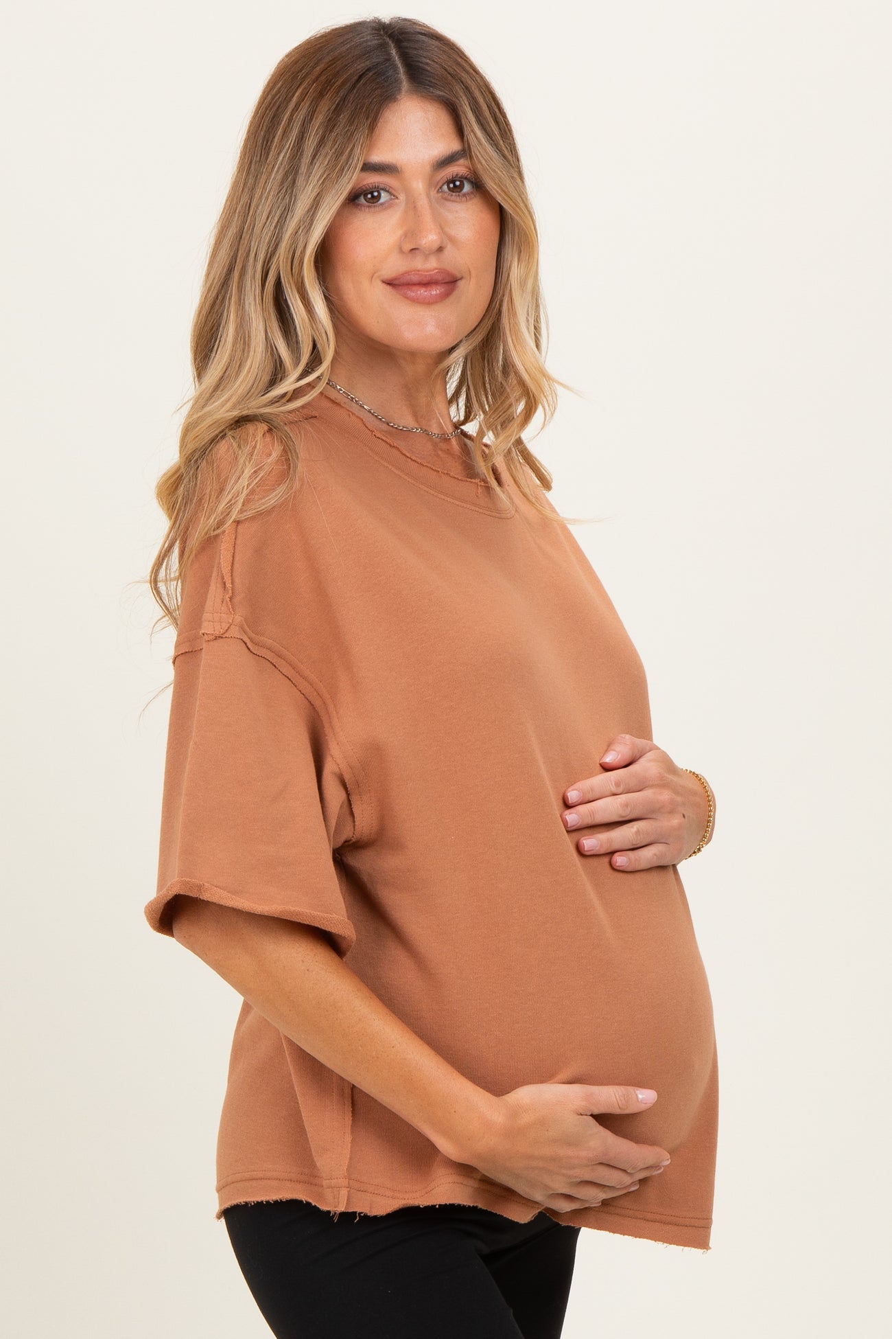 woman wearing a burnt orange oversized maternity t-shirt and cradling her baby bump