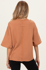 woman wearing a rust-colored oversized short sleeve maternity top with raw hem details, showing the back view
