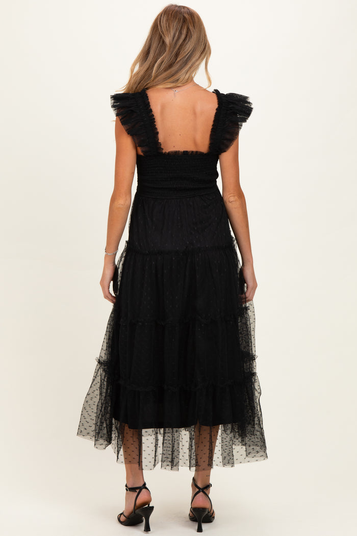 woman wearing a black tiered maternity dress with ruffled sleeves, showing a smocked back and sheer dotted fabric