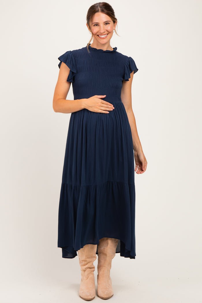 woman wearing a navy blue maternity maxi dress with short ruffled sleeves and a smocked bodice, showing her baby bump