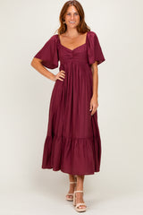 woman wearing a burgundy maxi dress with short sleeves and a tiered skirt, standing with a smile