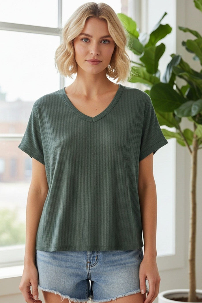 woman wearing a dark green short sleeve v-neck top paired with light denim shorts in a bright indoor setting