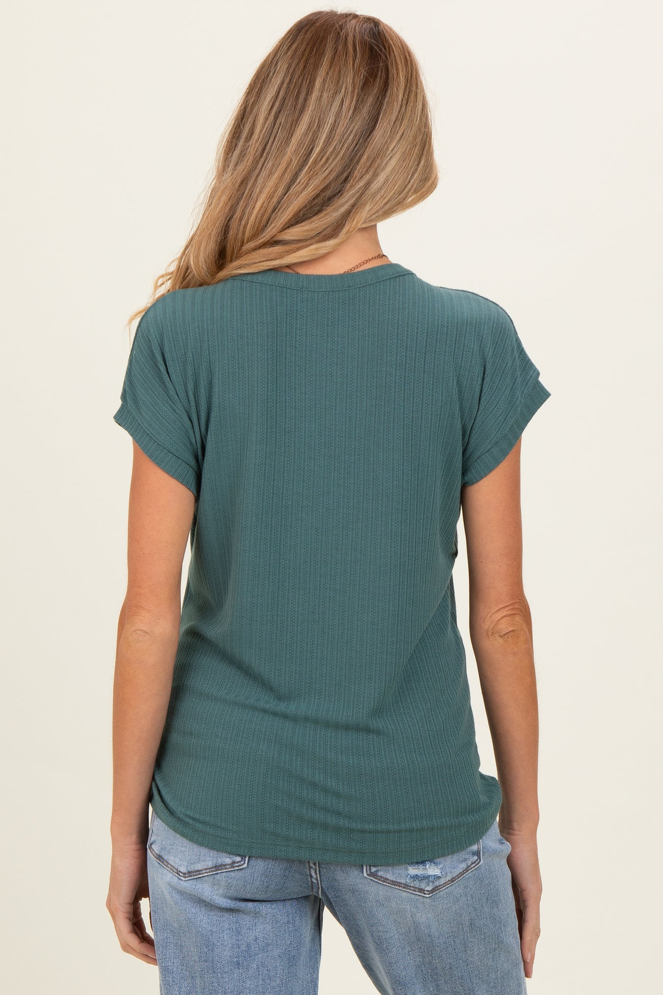 woman wearing a green ribbed maternity top, view from the back, paired with light blue jeans
