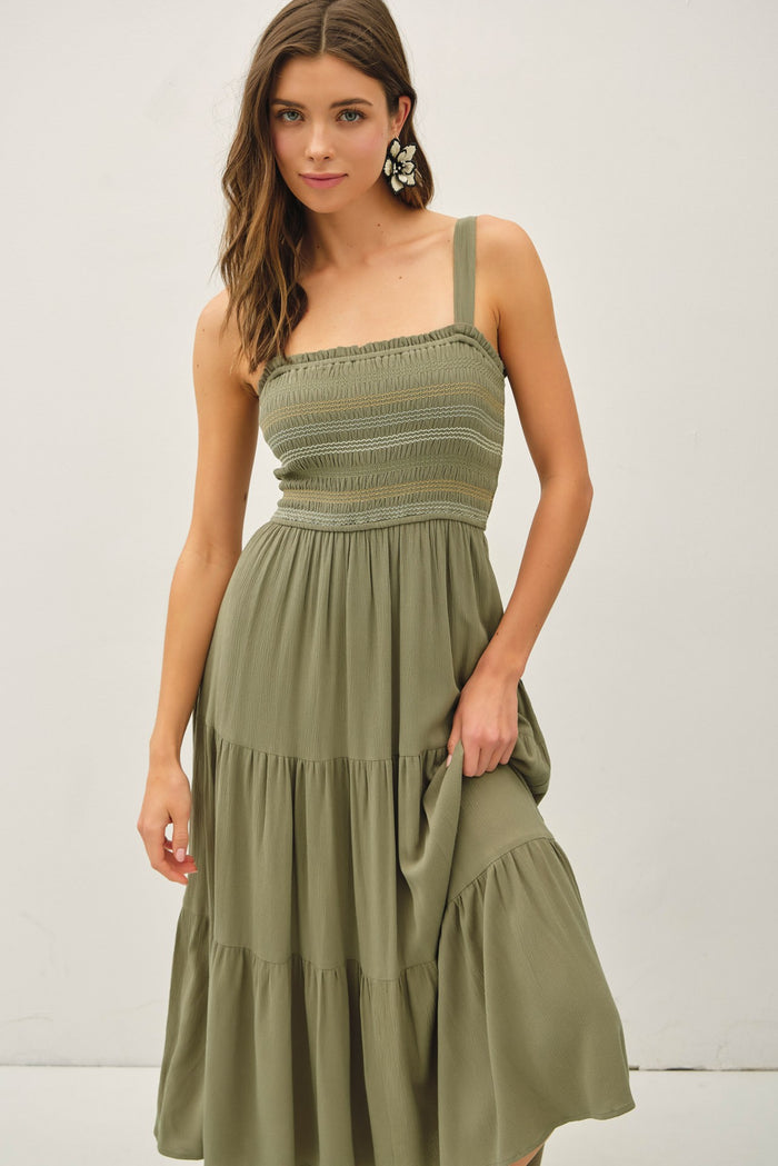 woman wearing a sage green smocked midi dress with a tiered skirt and wide straps