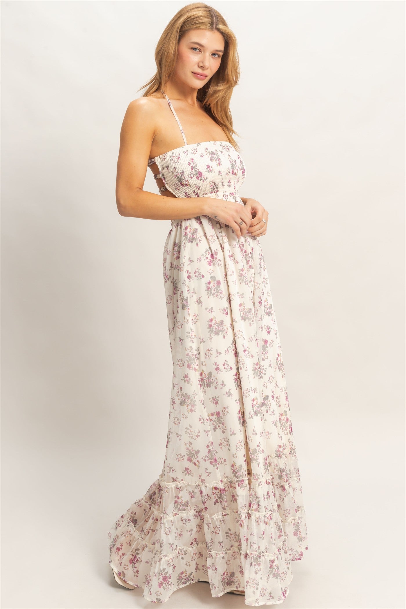 woman wearing a white floral maxi dress with a fitted bodice and ruffled hemline, posing against a neutral background