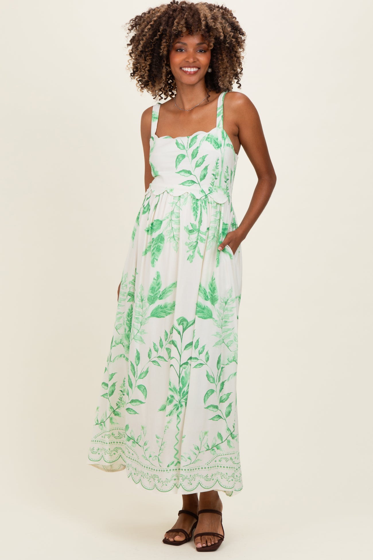 woman wearing a floral green and white maxi maternity dress with adjustable straps and pockets