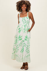 woman wearing a floral green and white maxi maternity dress with adjustable straps and pockets