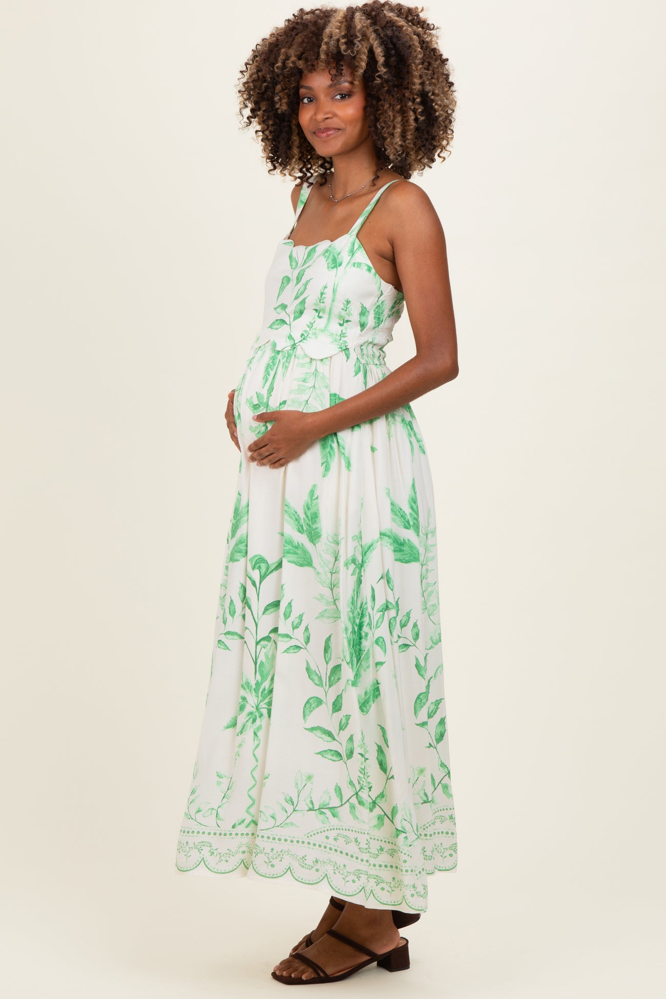 woman wearing a white maternity maxi dress with green leafy print and a visible baby bump