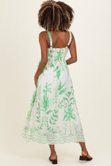 woman wearing a white maternity maxi dress with green leaf patterns and adjustable straps, showing a baby bump