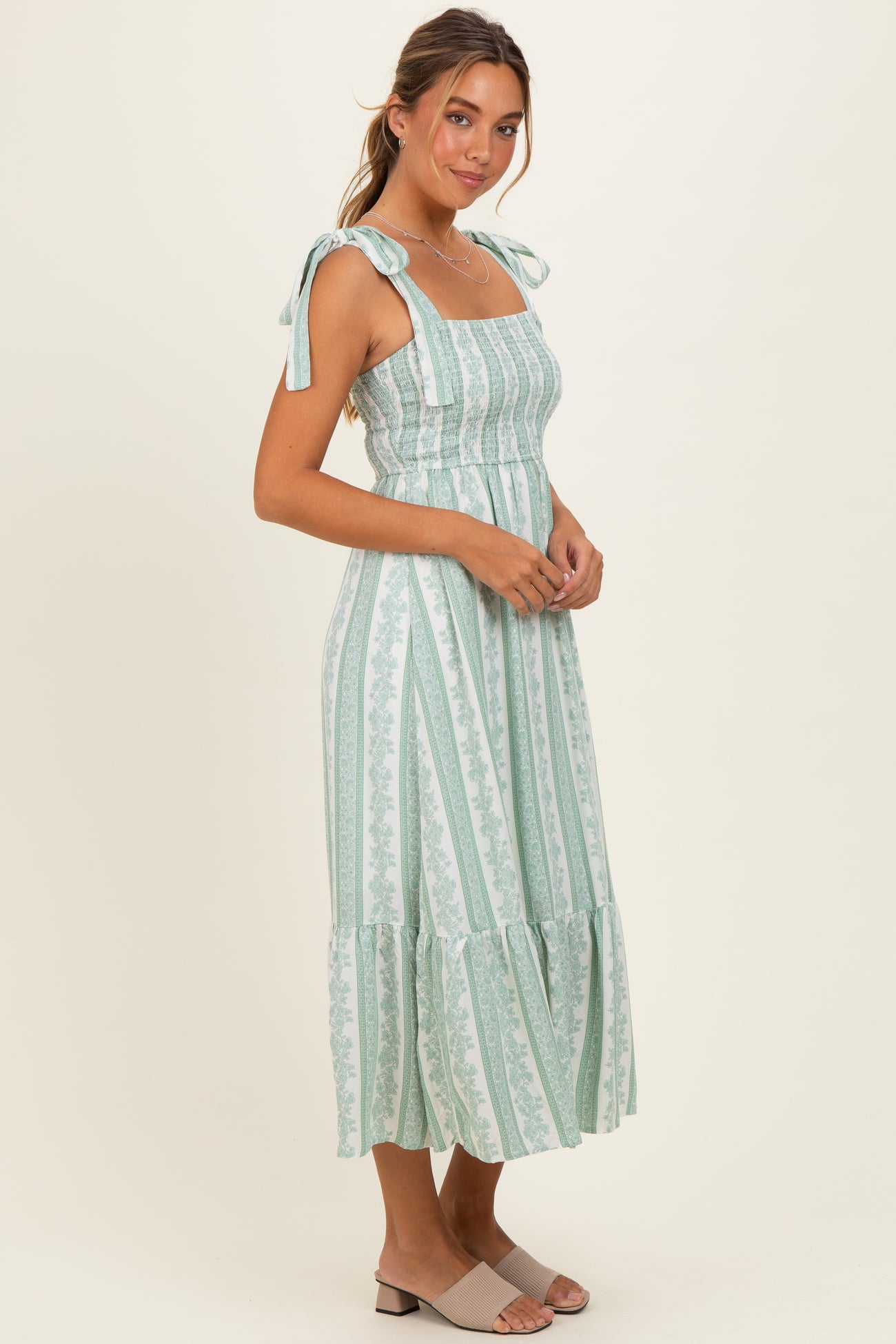 woman wearing a mint green stripe midi dress with adjustable tie straps and a ruffled hem
