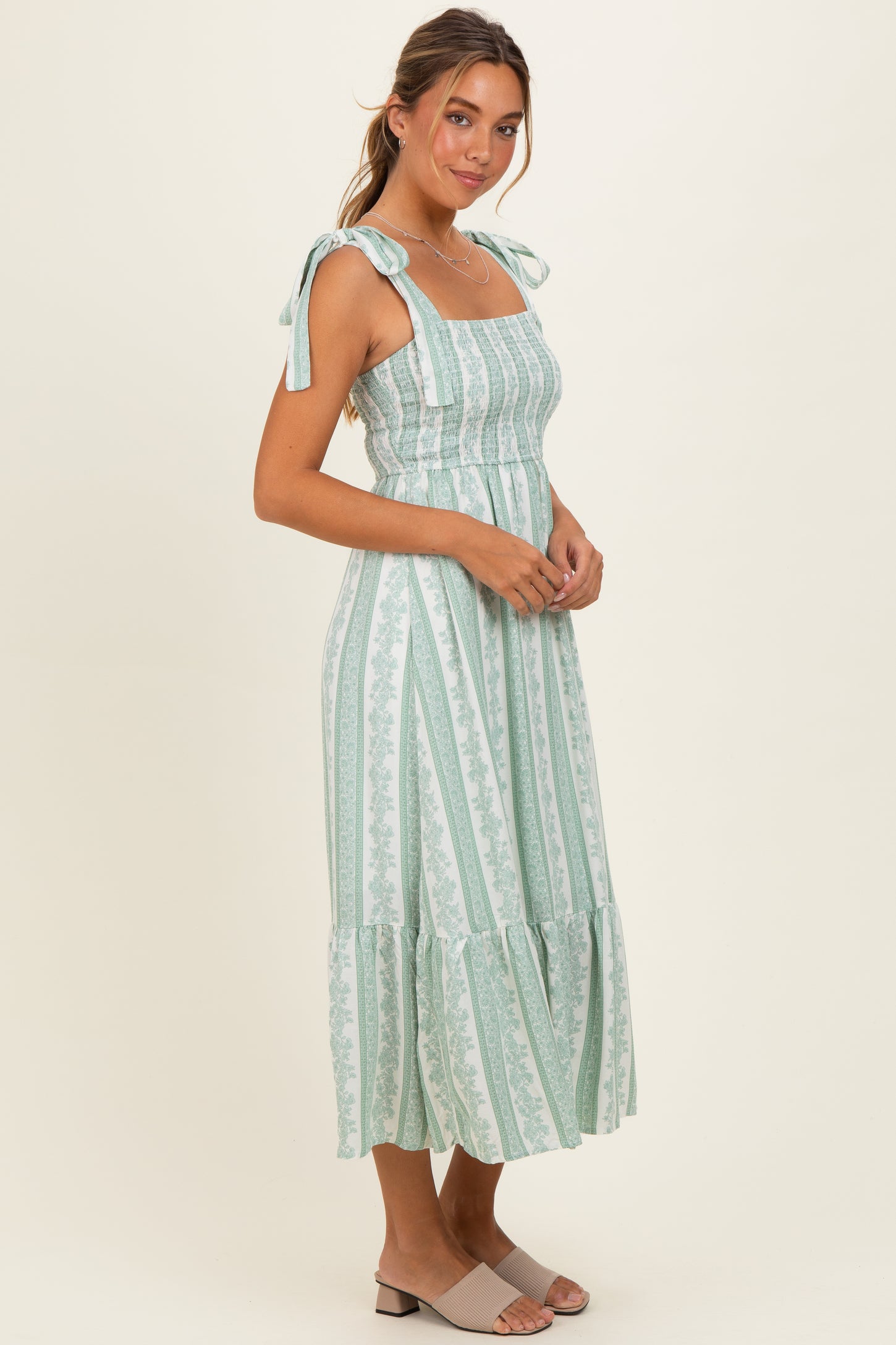 woman wearing a mint green stripe midi dress with adjustable tie straps and a ruffled hem