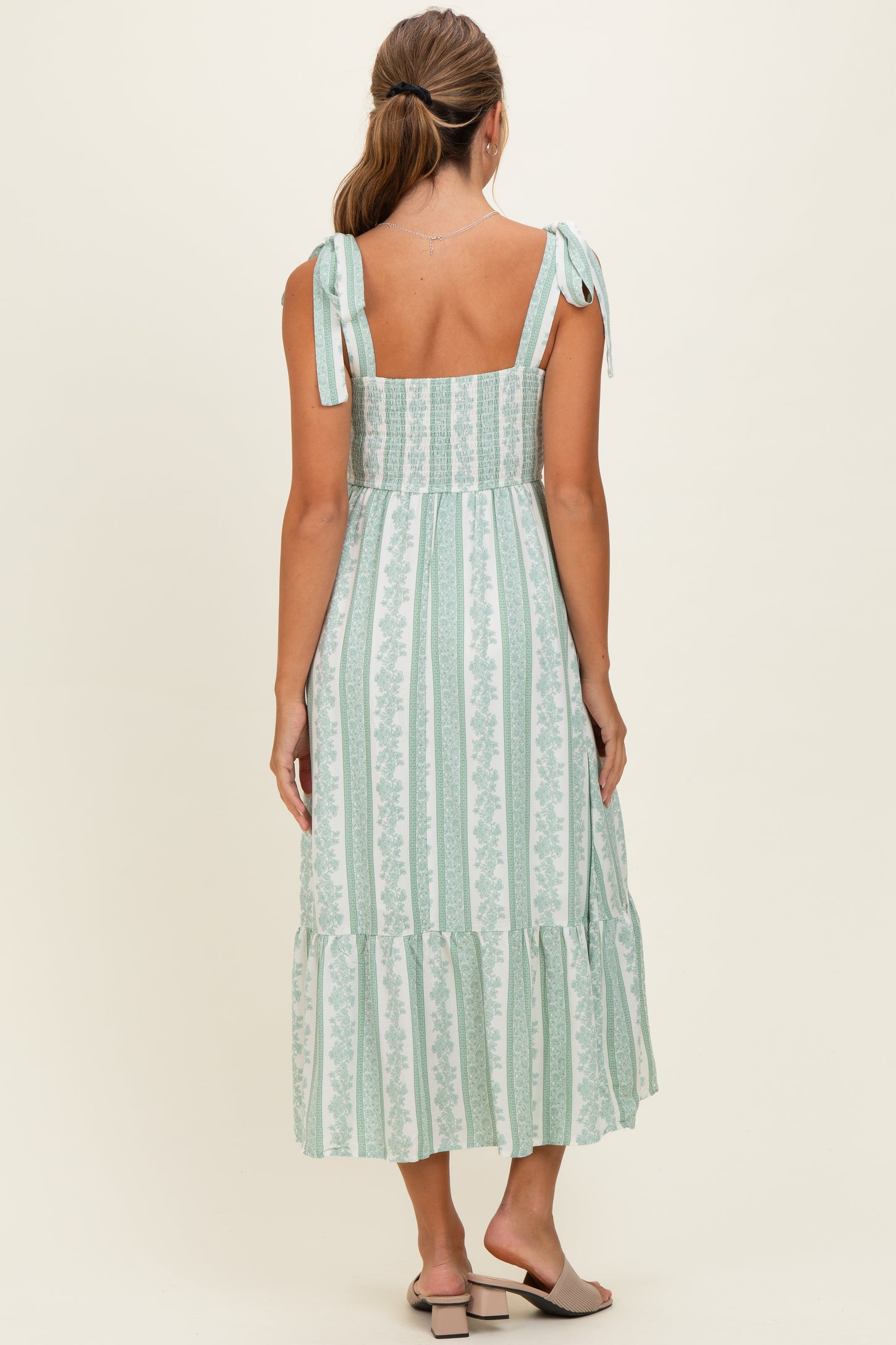 woman wearing a green and white striped maxi dress with tie straps and a ruffled hem, shown from the back