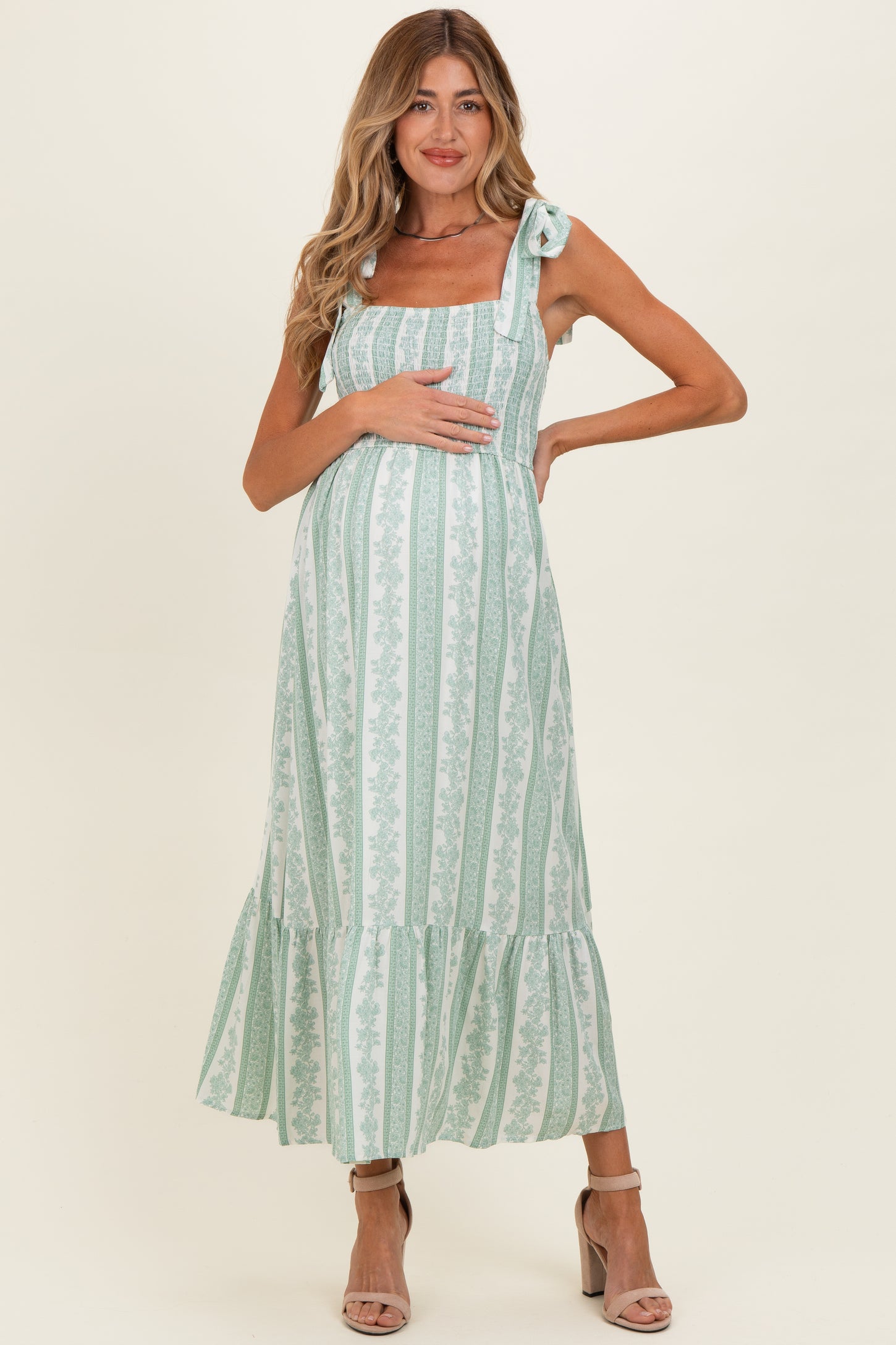 woman wearing a green striped maternity dress with tied straps and a ruffled hem, holding her baby bump