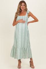 woman wearing a green striped maternity dress with tied straps and a ruffled hem, holding her baby bump