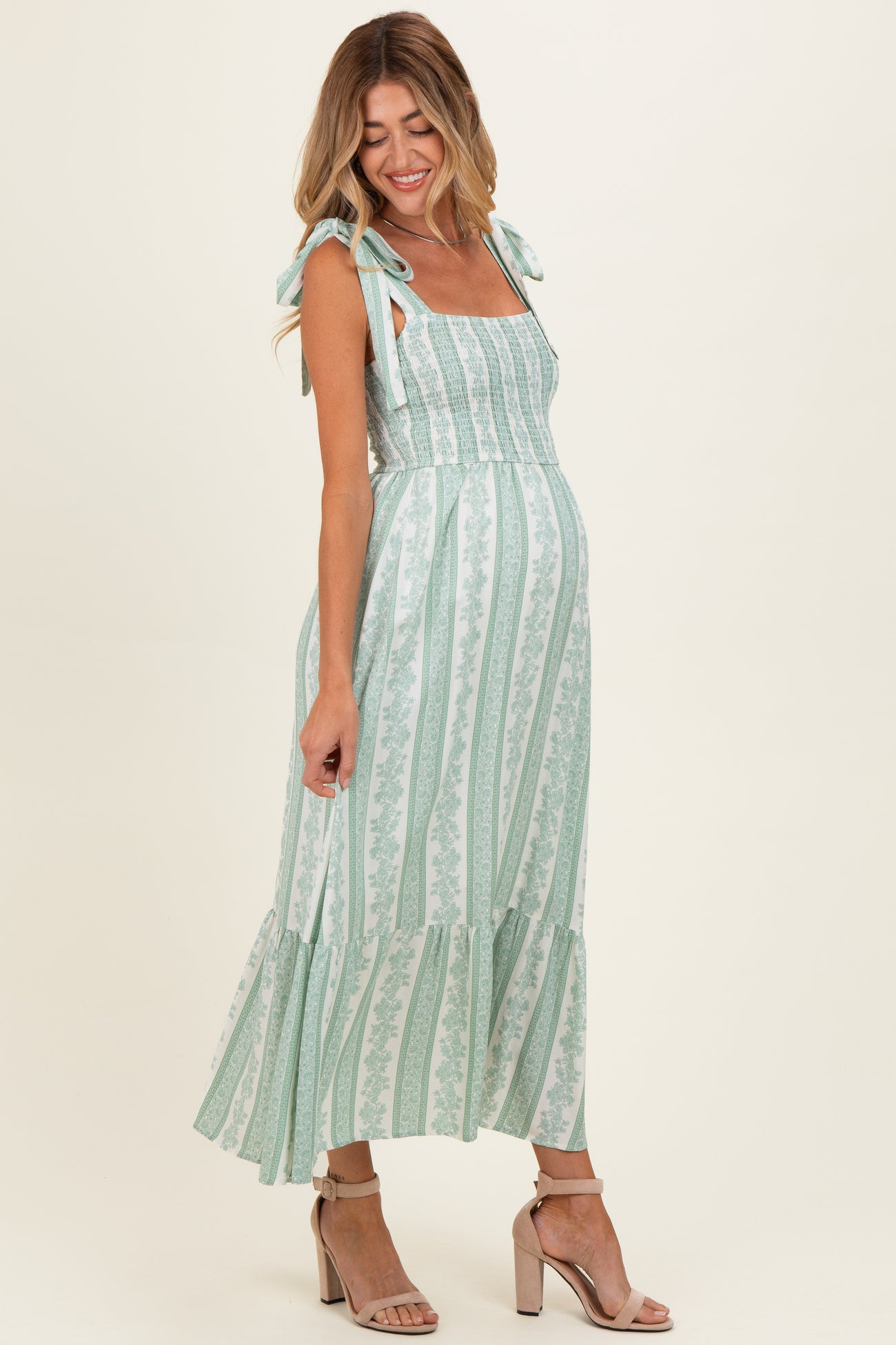 woman wearing a green and white striped maternity dress with tie straps and a flowing skirt, showing her baby bump
