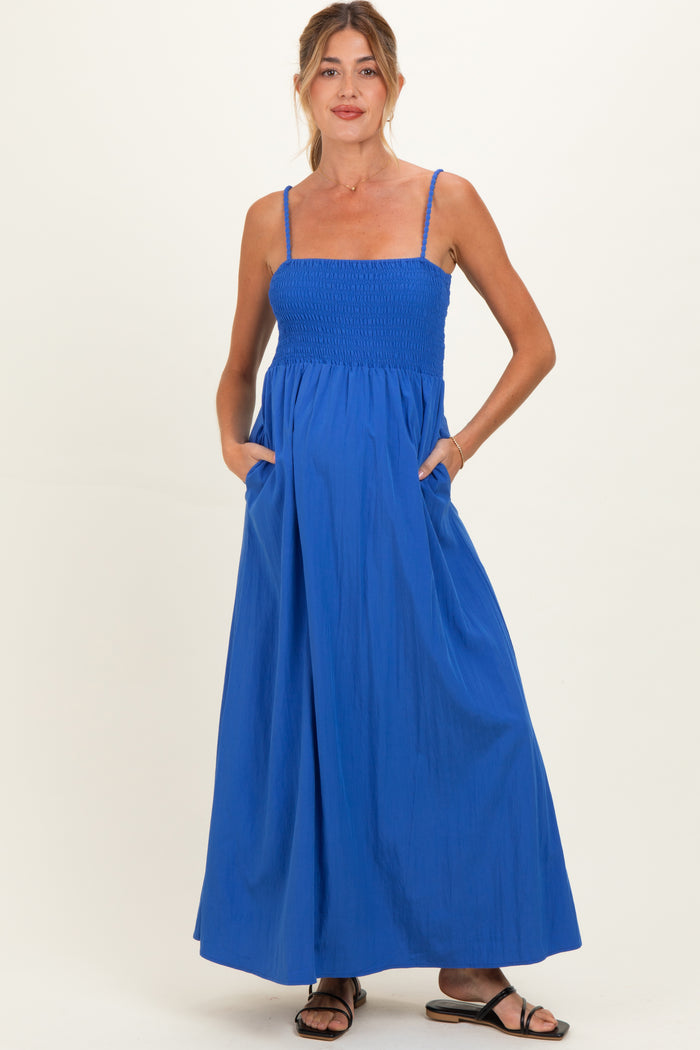 woman wearing a bright blue maternity maxi dress with smocked bodice and pockets, featuring spaghetti straps and a flowing skirt