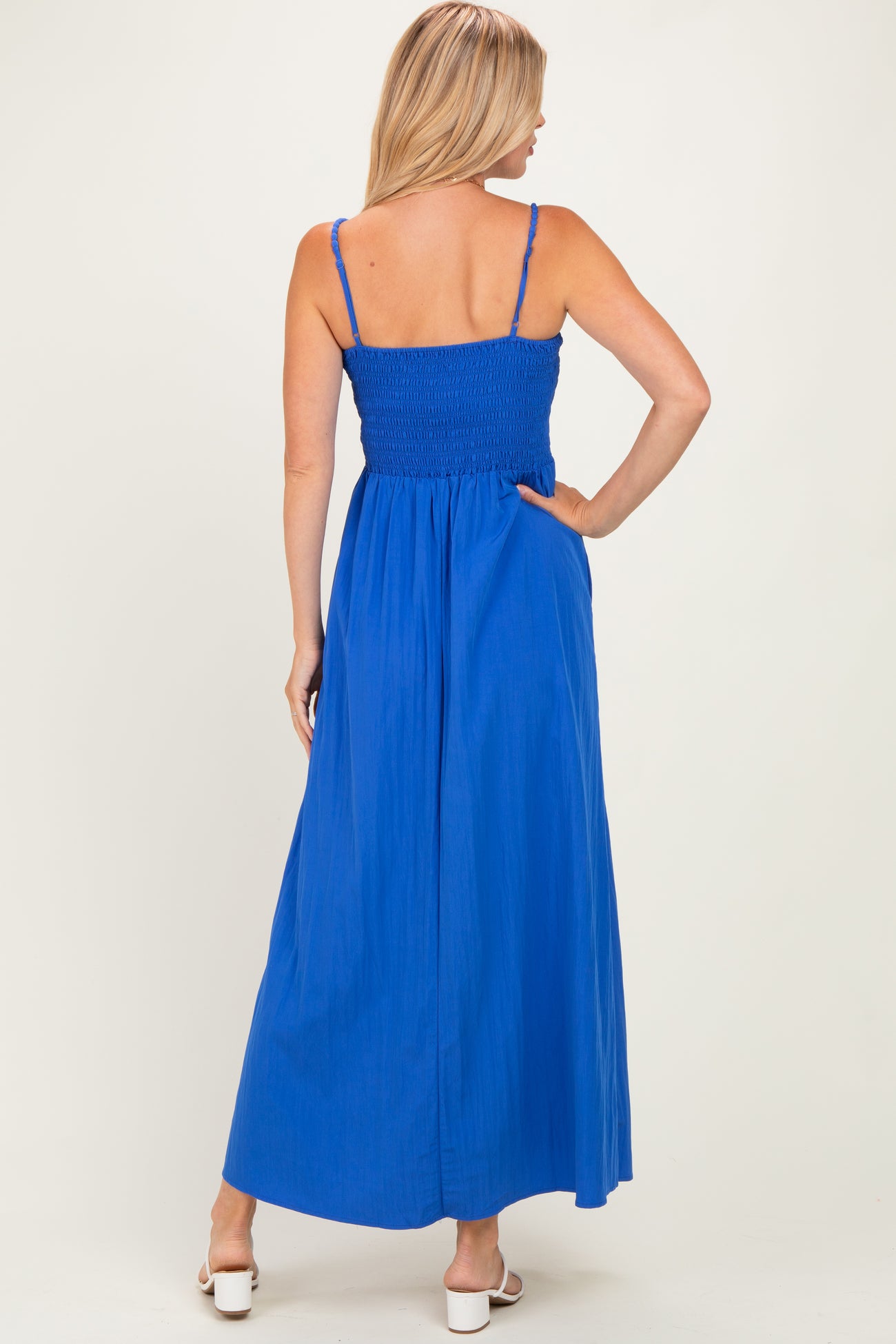 woman wearing a back view of a bright blue maxi dress with smocked bodice and adjustable straps