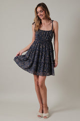 woman wearing a navy floral sundress with adjustable straps and a fitted bodice, smiling and holding the skirt out gently