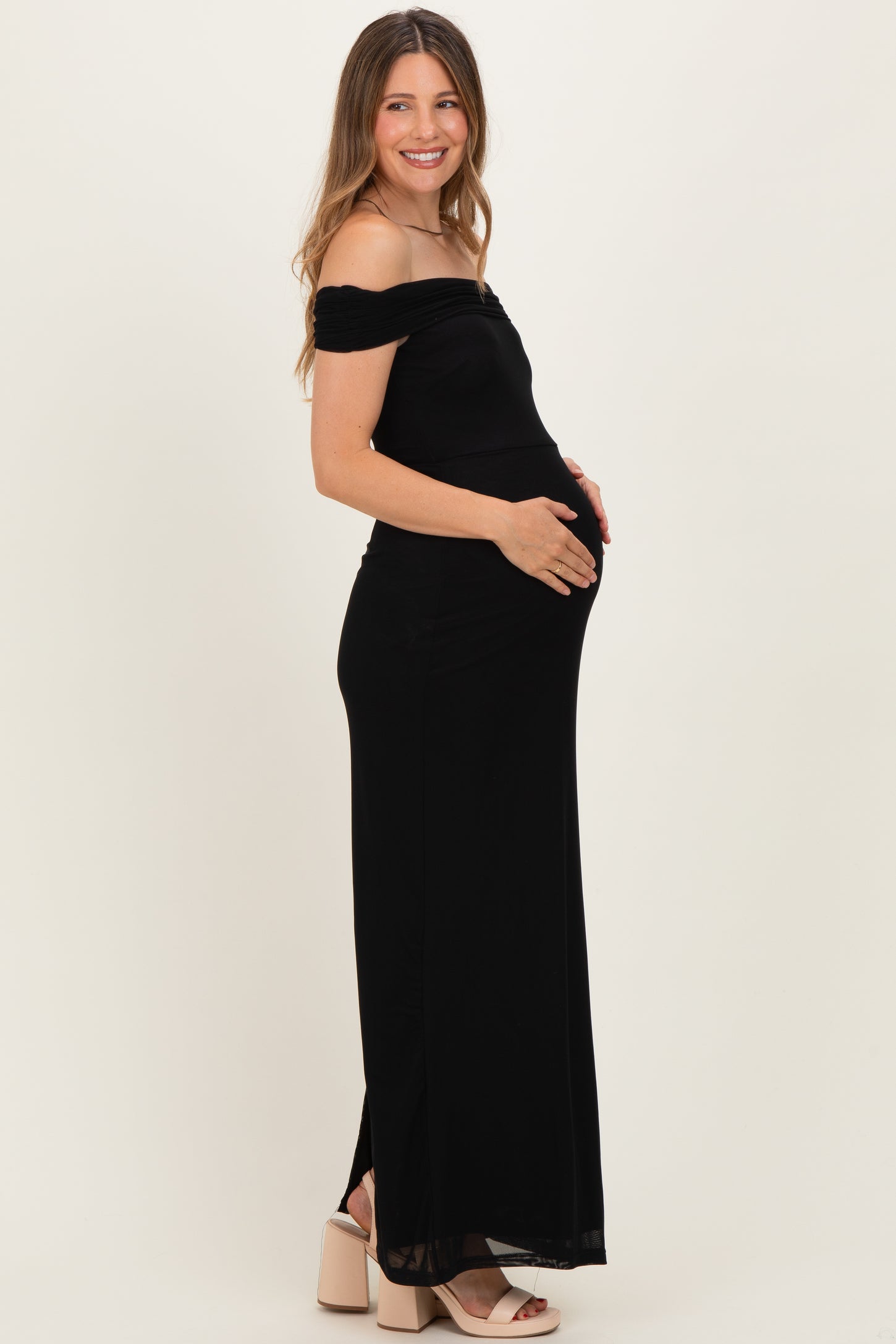 woman wearing a black off-the-shoulder maternity gown and holding her baby bump