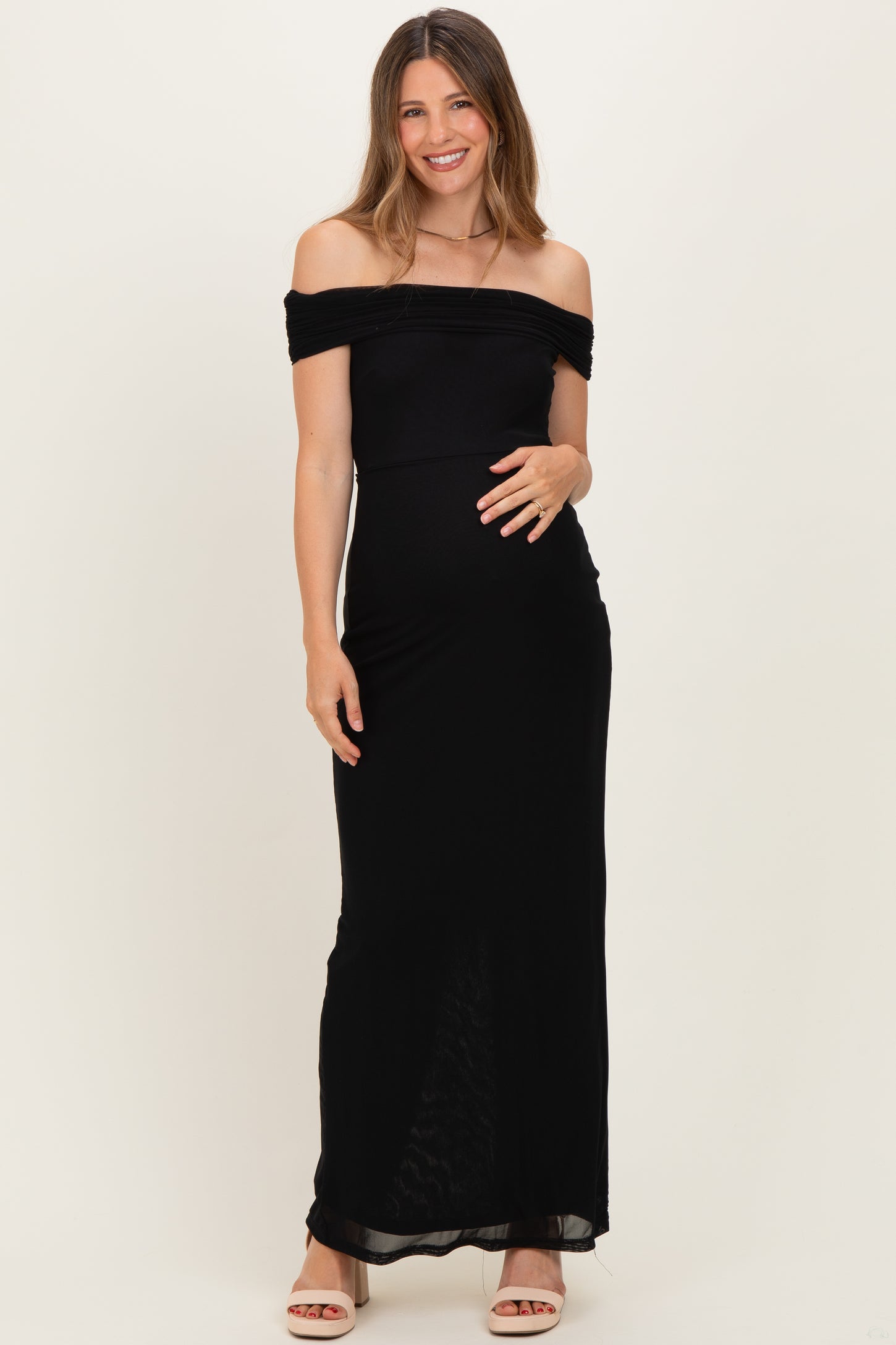woman wearing a black off-shoulder maternity dress with a fitted silhouette and holding her baby bump