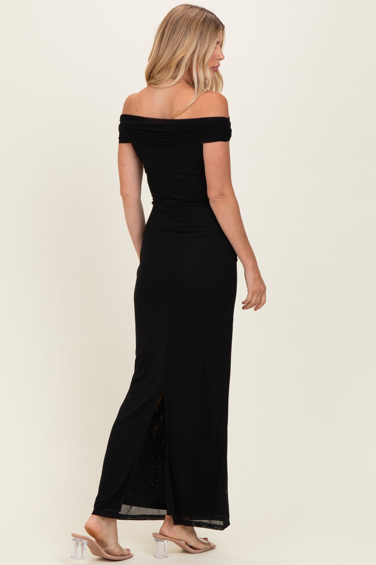 woman wearing a black off-the-shoulder maxi dress with a side slit and strappy heels, posing from the back